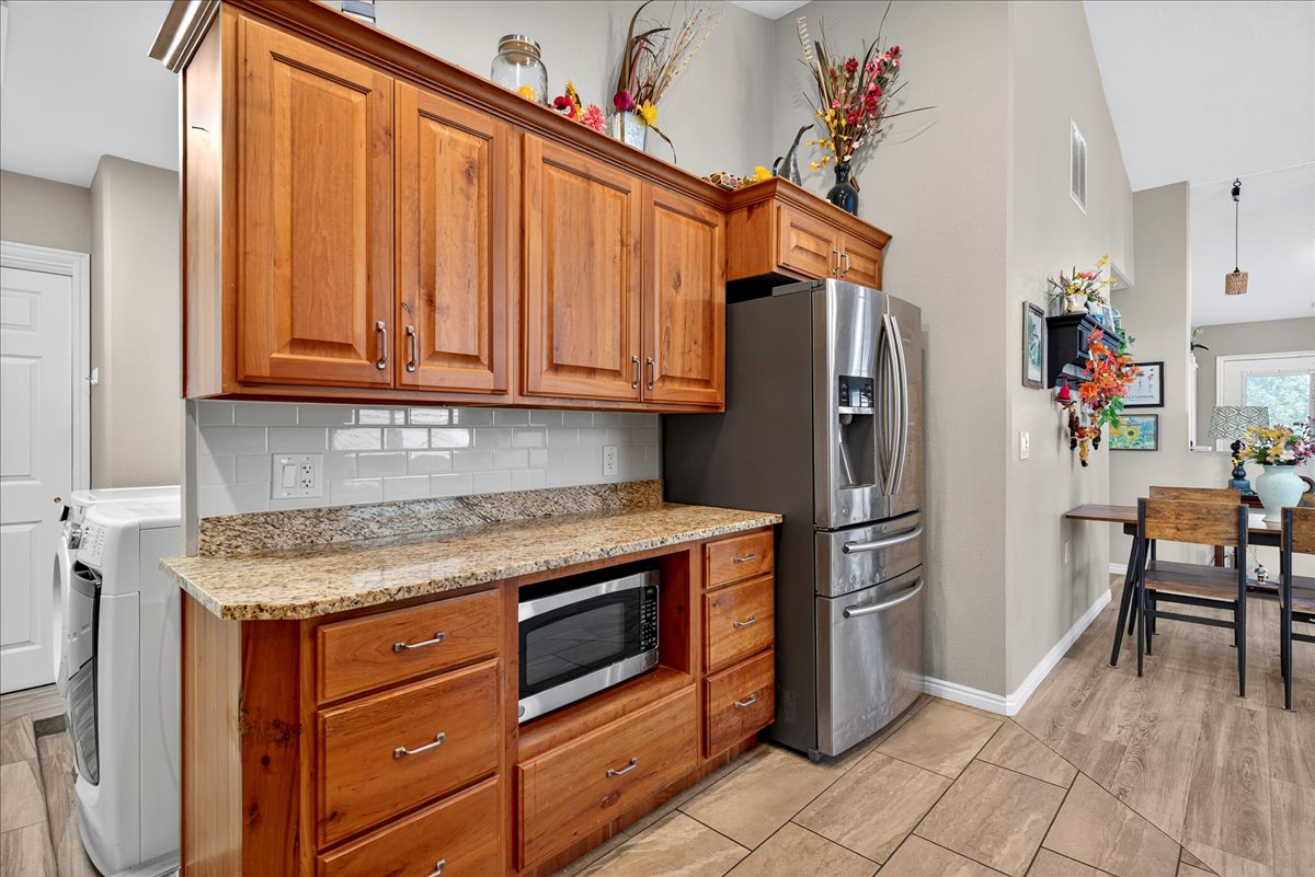 Kitchen with wood finish cabinets, light stone countertops, tasteful backsplash, stainless steel appliances, and washer / clothes dryer