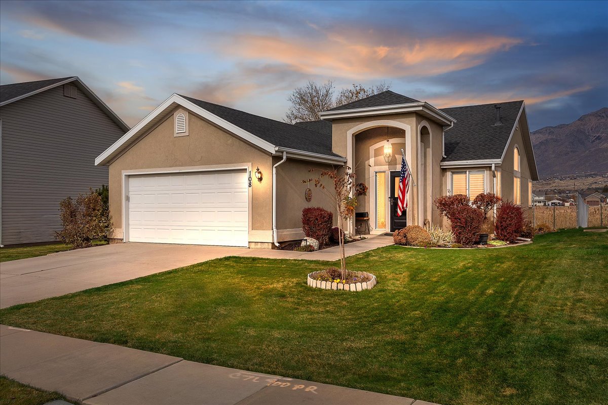 View of front facade featuring stucco siding, an attached garage, a front yard, and driveway