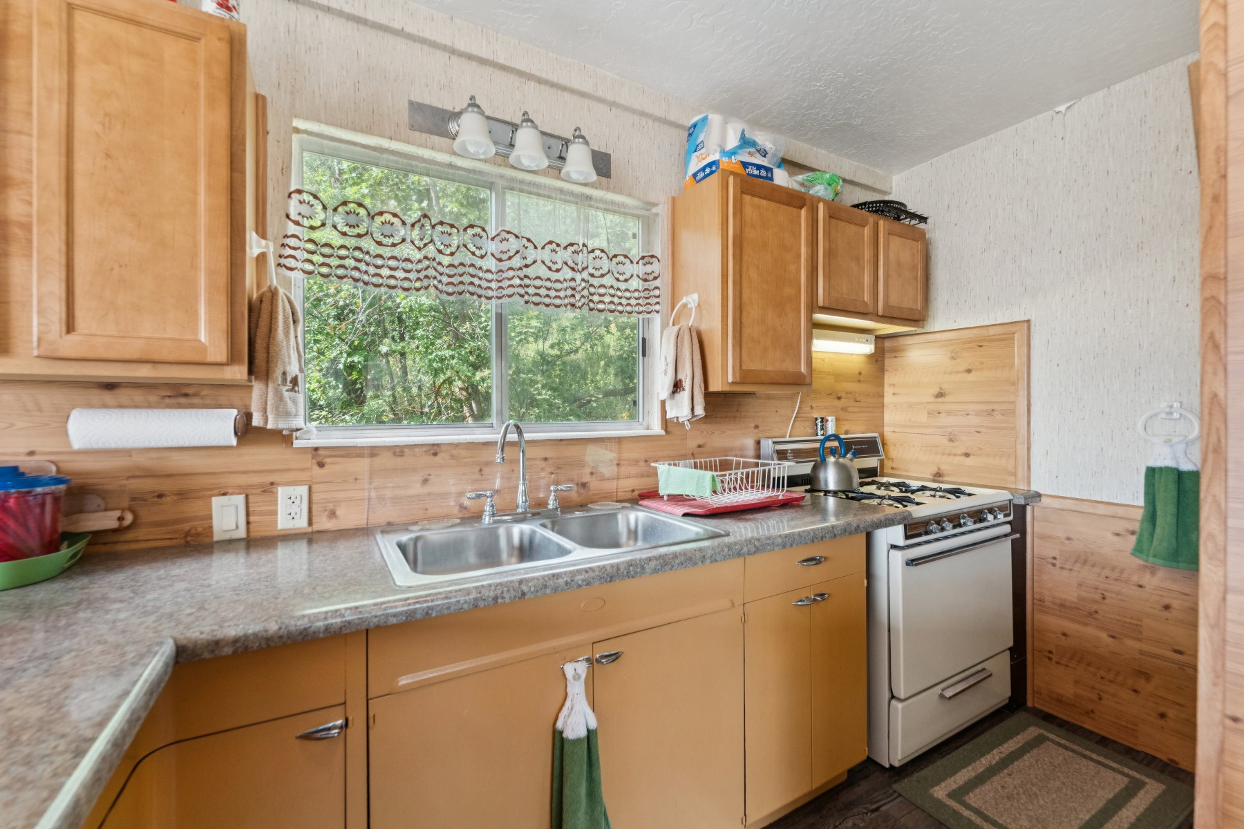 Kitchen featuring gas range gas stove, wooden walls, a textured ceiling, wallpapered walls, and light countertops