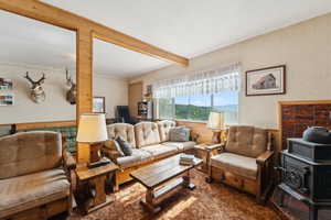 Living room with beamed ceiling, wallpapered walls, dark wood-type flooring, and a textured ceiling