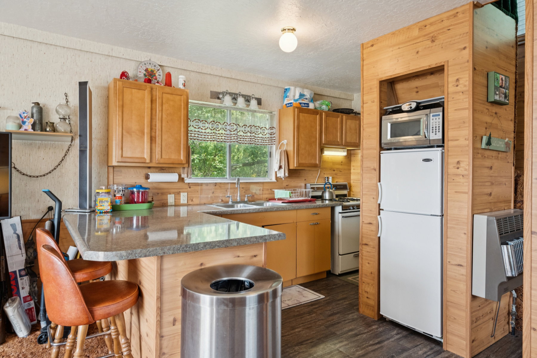 Kitchen featuring a peninsula, white appliances, a kitchen bar, dark wood-style flooring, and a textured ceiling