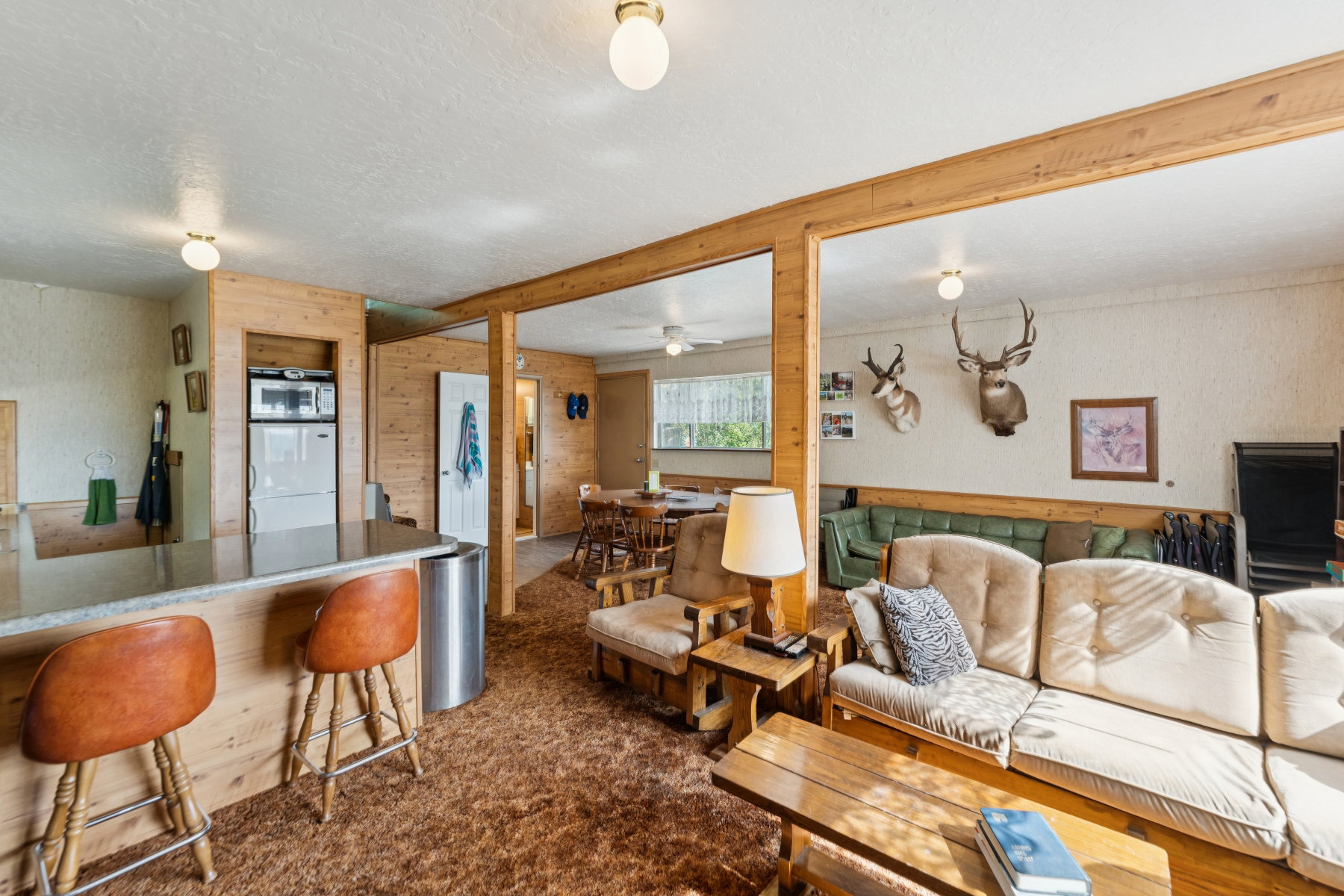 Living area with dark colored carpet, wood walls, a textured ceiling, a ceiling fan, and wallpapered walls