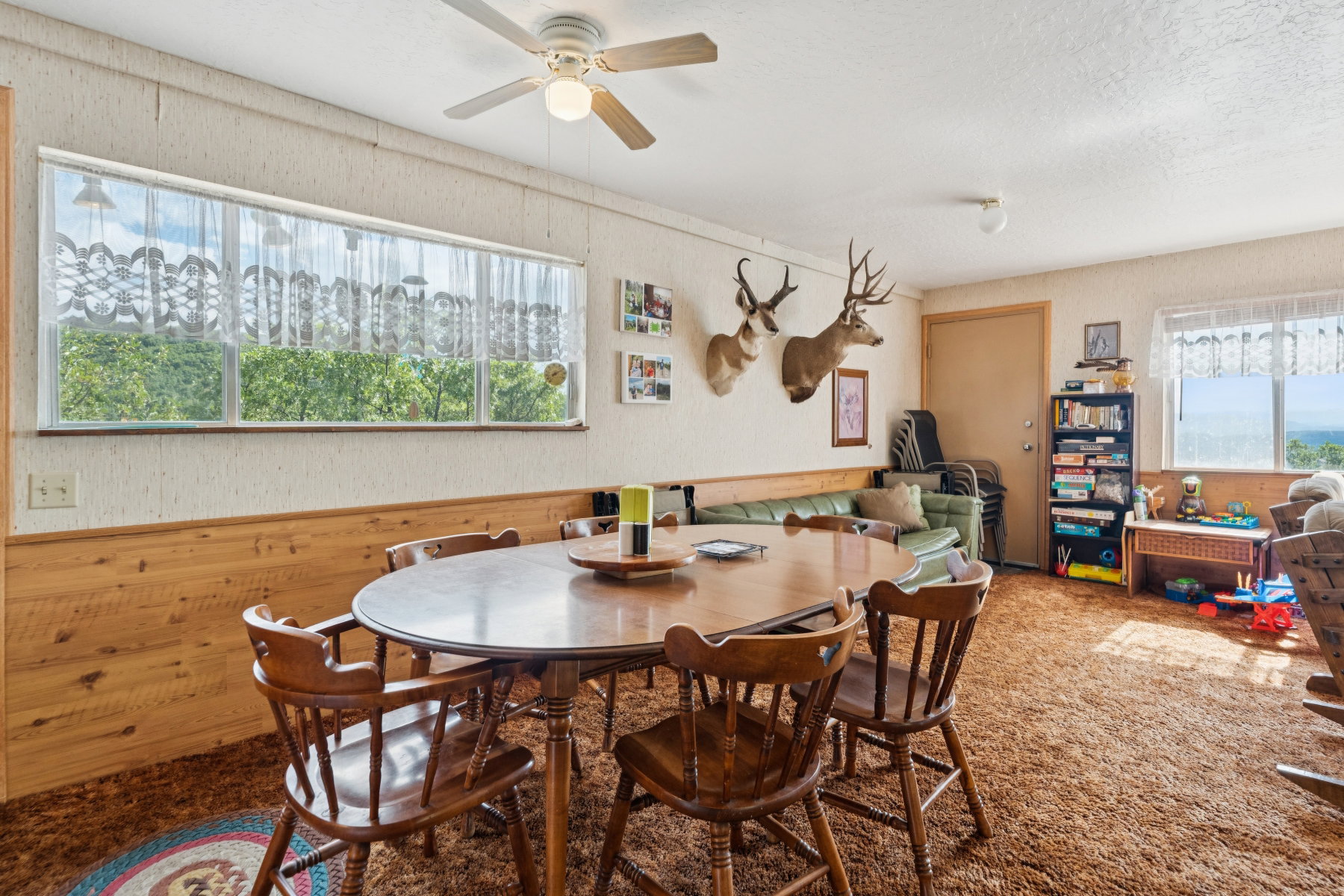 Carpeted dining area featuring ceiling fan and wooden walls