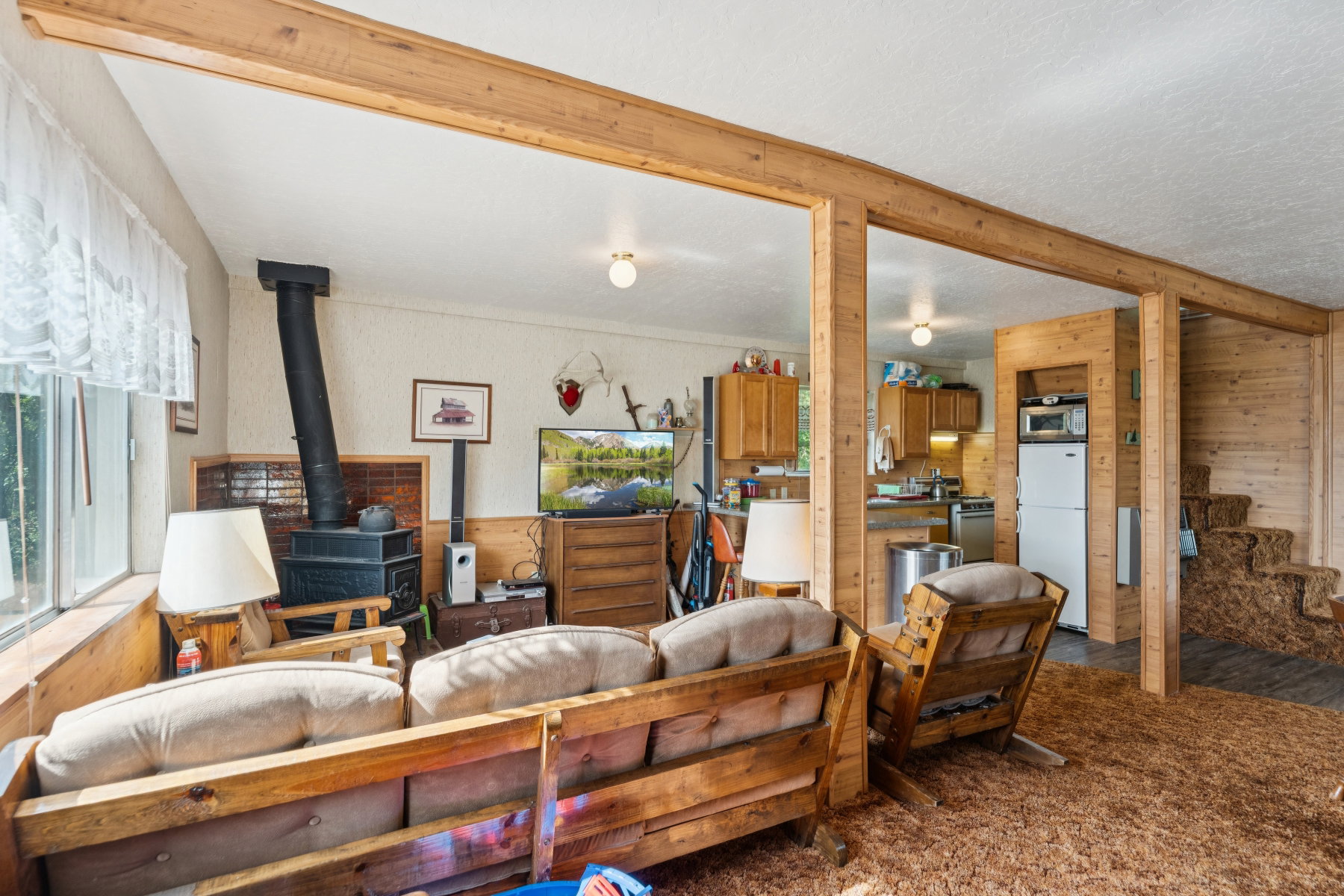 Living room with wood walls, dark colored carpet, a wood stove, and beam ceiling