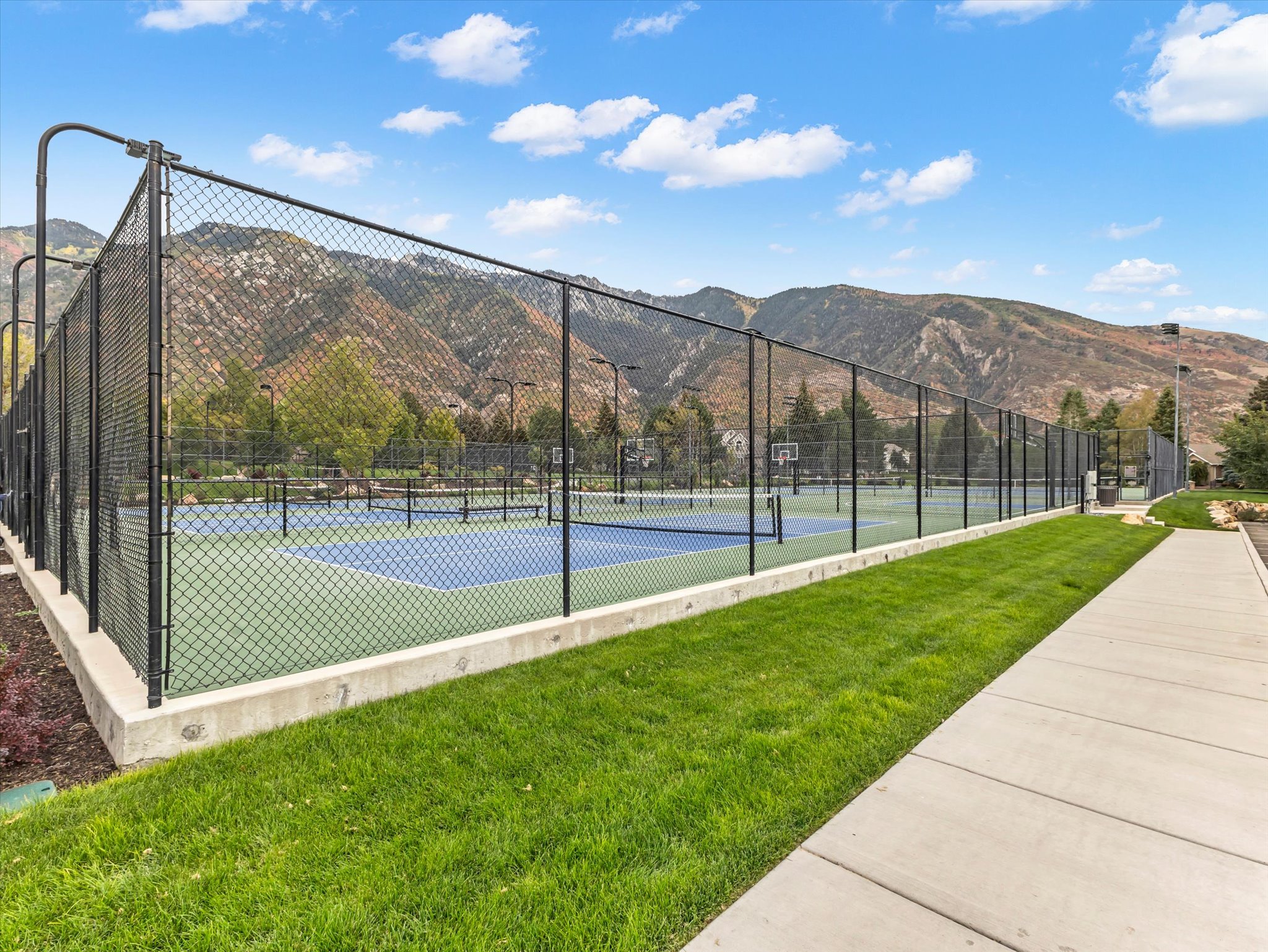 Multiple sports courts featuring blue and green surfacing, black chain-link fencing, and integrated lighting