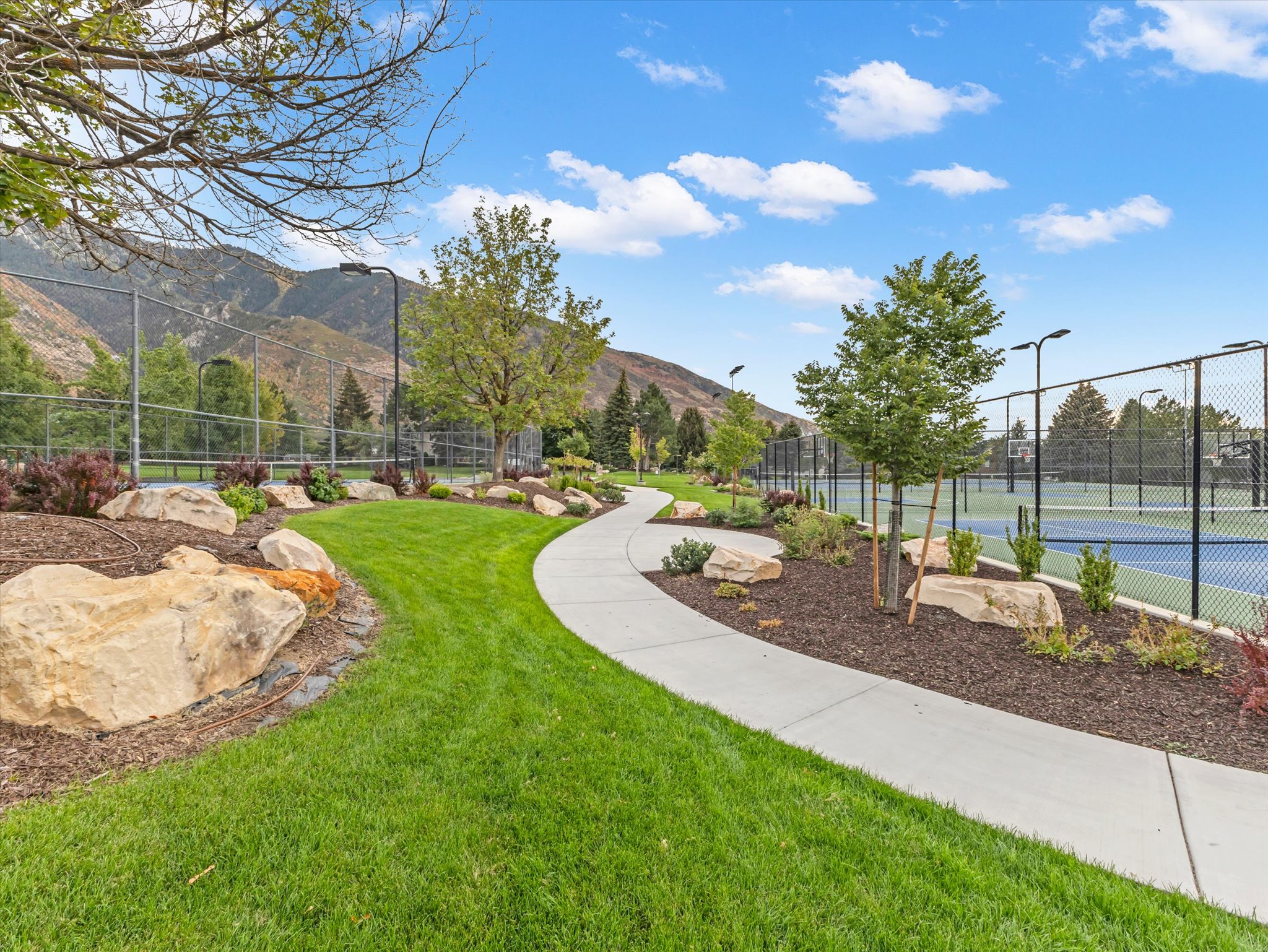 Curved concrete pathway bordered by landscaped beds with natural rock accents and mature plantings