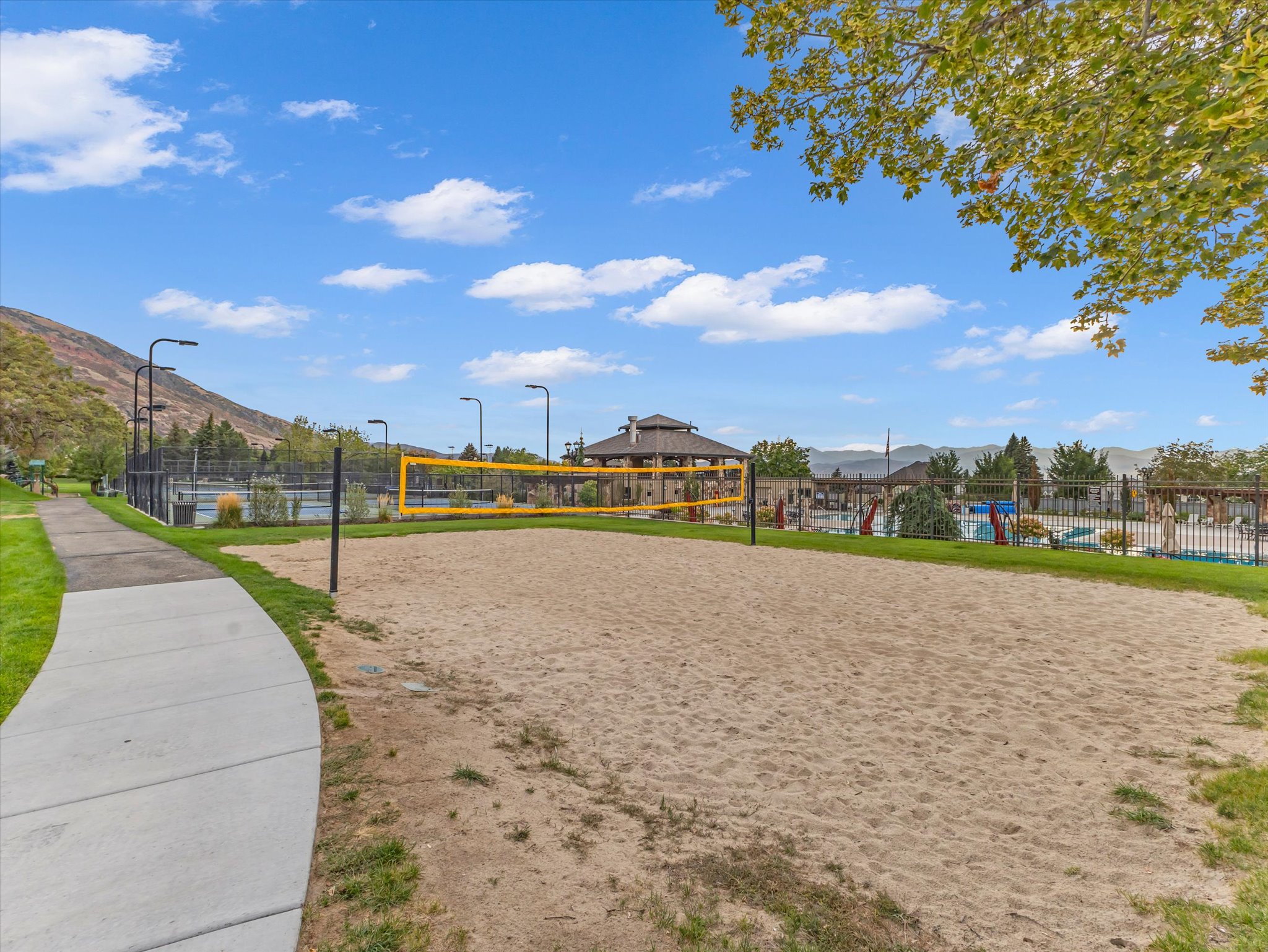 Sand volleyball court with a yellow net, bordered by green grass and a concrete pathway