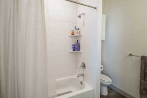 Bathroom with toilet and shower / bathtub combination with curtain