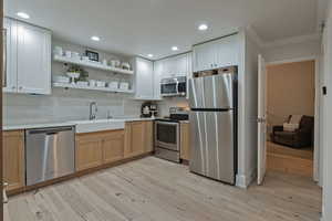 Kitchen with stainless steel appliances, open shelves, recessed lighting, backsplash, and light wood finished floors