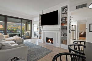 Living room featuring light wood finished floors, ornamental molding, built in shelves, and a fireplace