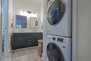 Laundry area featuring stacked washer / dryer, light wood finished floors, and crown molding