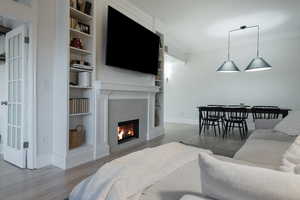 Living area with light wood finished floors, ornamental molding, a tile fireplace, and built in shelves