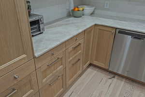 Kitchen with light stone countertops, stainless steel dishwasher, light wood-style flooring, and tasteful backsplash
