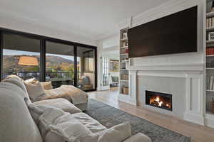 Living room featuring light wood-style floors, ornamental molding, a tile fireplace, and built in features