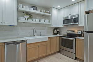 Kitchen with stainless steel appliances, backsplash, light wood finished floors, light stone counters, and open shelves