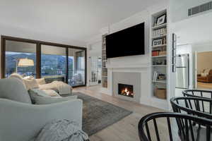 Living area with light wood-style floors, crown molding, a lit fireplace, and built in shelves