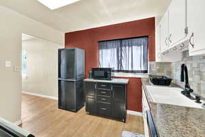 Kitchen with light wood-style flooring, backsplash, black microwave, a textured wall, and white cabinets