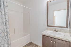 Bathroom with vanity, a textured wall, shower / tub combo with curtain, and light wood-style flooring