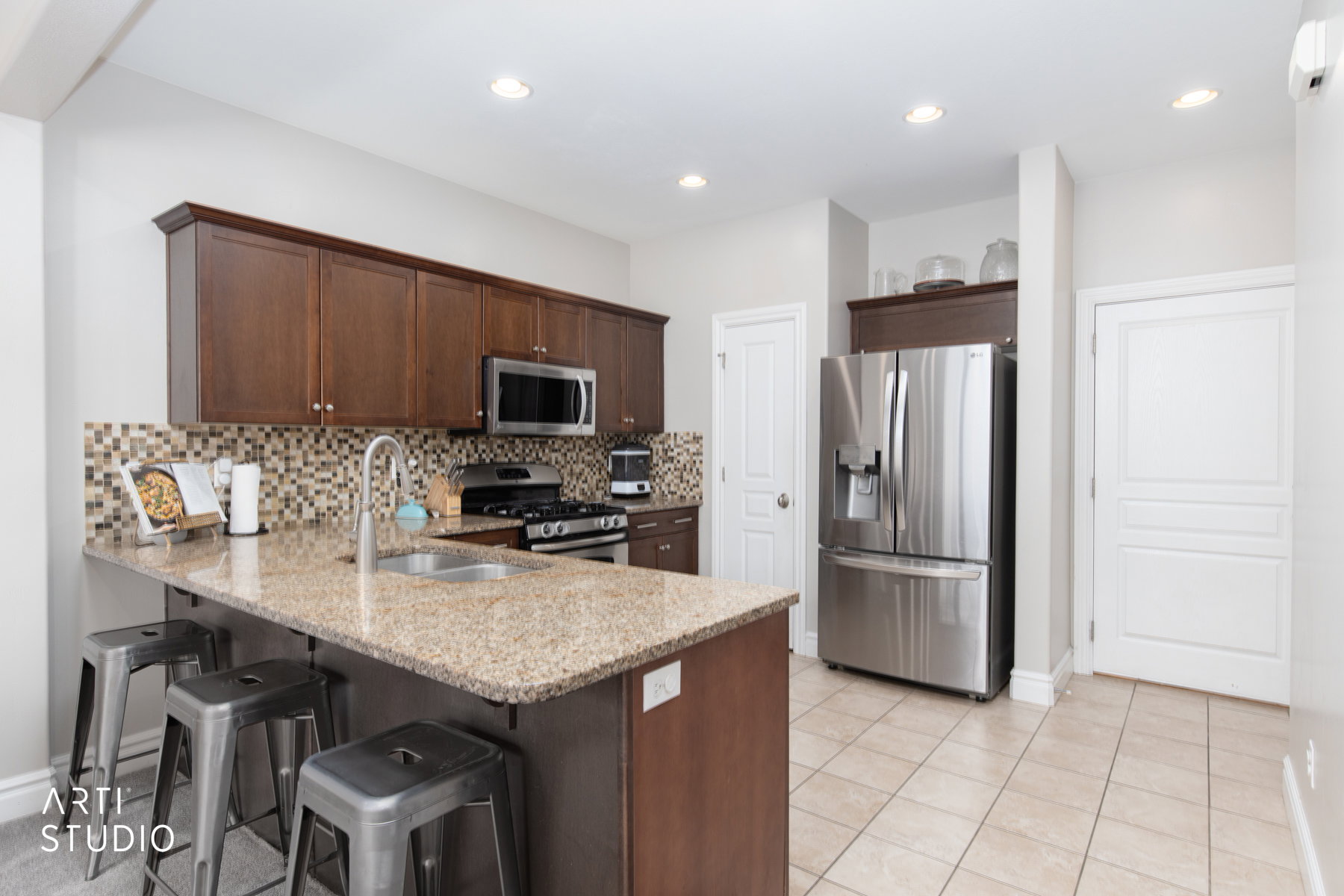 Kitchen with dark wood finish cabinets, stainless steel appliances, light stone countertops, a peninsula, and a breakfast bar area