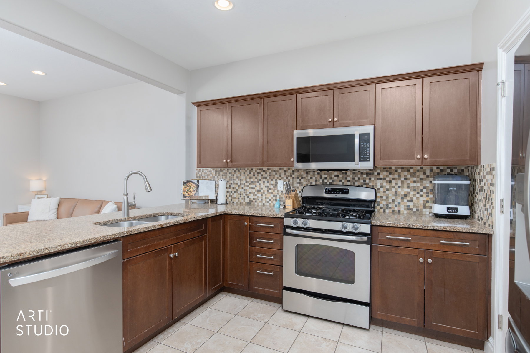 Kitchen with stainless steel appliances, light stone counters, decorative backsplash, a peninsula, and light tile patterned floors