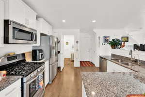 Kitchen with stainless steel appliances, dark stone countertops, white cabinetry, light wood finished floors, and recessed lighting