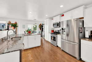Kitchen featuring stainless steel appliances, dark stone countertops, white cabinetry, light wood-style flooring, and hanging light fixtures