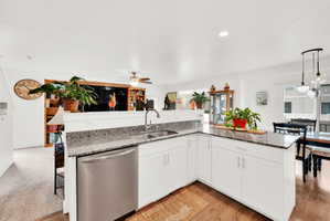 Kitchen featuring dark stone counters, white cabinets, open floor plan, dishwasher, and hanging light fixtures