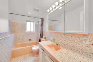 Full bath with vanity, tile walls, shower / bath combination with curtain, and a wainscoted wall