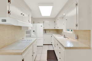 Kitchen with tile counters, white cabinetry, white appliances, decorative backsplash, and light tile patterned floors