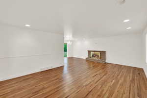Unfurnished living room with light wood finished floors, a glass covered fireplace, and recessed lighting