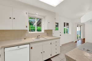 Kitchen with tile countertops, tasteful backsplash, white appliances, and white cabinetry