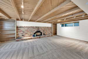 Unfurnished living room with light colored carpet, rail lighting, a brick fireplace, and a wooden ceiling with exposed beams