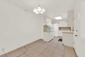 Kitchen with white fridge with ice dispenser, light tile patterned floors, white cabinetry, tile counters, and tasteful backsplash