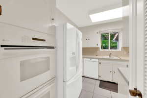 Kitchen featuring white appliances, white cabinetry, light countertops, light tile patterned floors, and backsplash