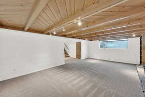 Carpeted empty room with track lighting and a wooden ceiling with exposed beams