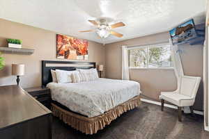 Bedroom featuring dark colored carpet, a textured ceiling, and a ceiling fan