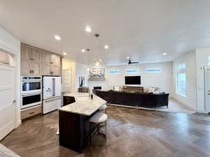 Dual tone kitchen featuring light stone countertops, a fireplace, white appliances, open floor plan, and a center island with sink
