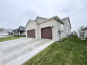 side of property with an attached garage, a lawn, driveway, and brick siding
