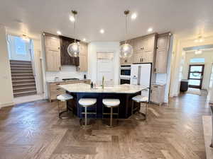 Kitchen featuring natural light, light stone counters, white appliances, a breakfast bar area, hardwood herringbone floors