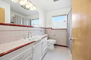 Bathroom featuring vanity, light tile patterned floors, tile walls, wainscoting, and a shower with shower curtain