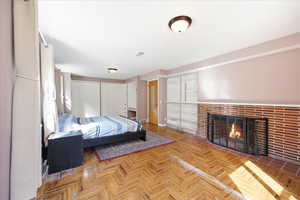 Bedroom featuring two closets, a brick fireplace, and parquet flooring