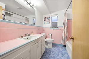 Full bathroom featuring vanity, wainscoting, tile walls, shower / bath combo, and dark tile patterned flooring