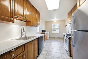 Kitchen with stainless steel appliances, wood finish cabinetry, light countertops, and light tile patterned floors