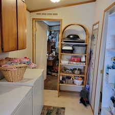 Laundry area featuring light floors, washing machine and dryer, crown molding, and cabinet space