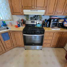 Kitchen with stainless steel range with gas stovetop, light countertops, and wood finish cabinets