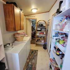Laundry area with light flooring, cabinet space, washer and clothes dryer, and crown molding