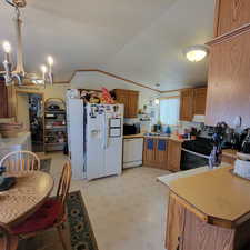 Kitchen with wood finish cabinetry, white appliances, light flooring, light countertops, and suspended lighting