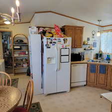 Kitchen featuring light floors, crown molding, hanging light fixtures, wood finish cabinetry, and white appliances