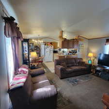Living area with suspended lighting, light colored carpet, and crown molding