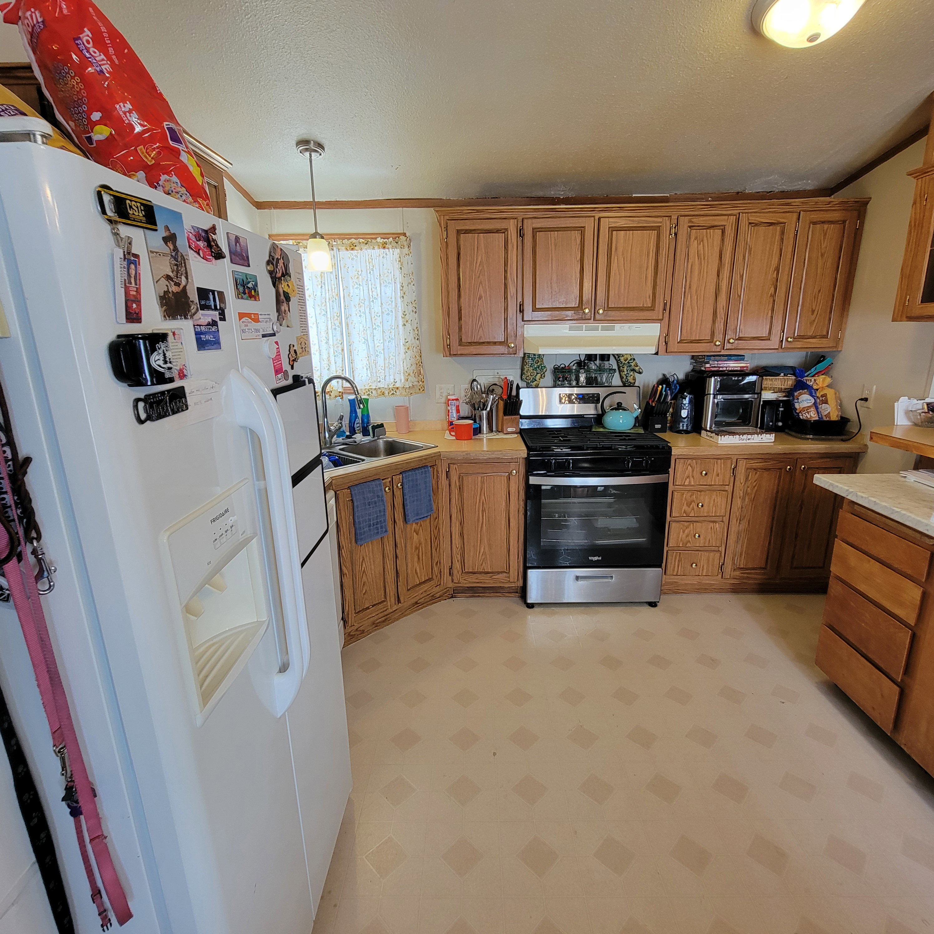 Kitchen featuring light flooring, light countertops, white refrigerator with ice dispenser, stainless steel gas stove, and wood finish cabinets